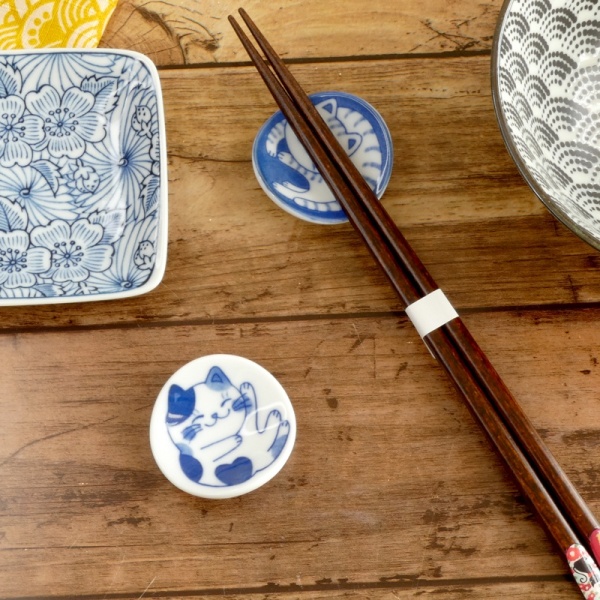 Two types of Nekochigura cat-themed chopstick rests on a table with plates and chopsticks