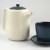 White Japanese teapot with blue lid next to a matching blue Japanese cup and saucer